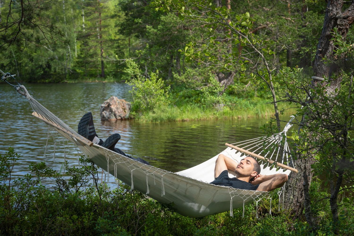 En kille som ligger och njuter i en hängmatta intill en sjö.