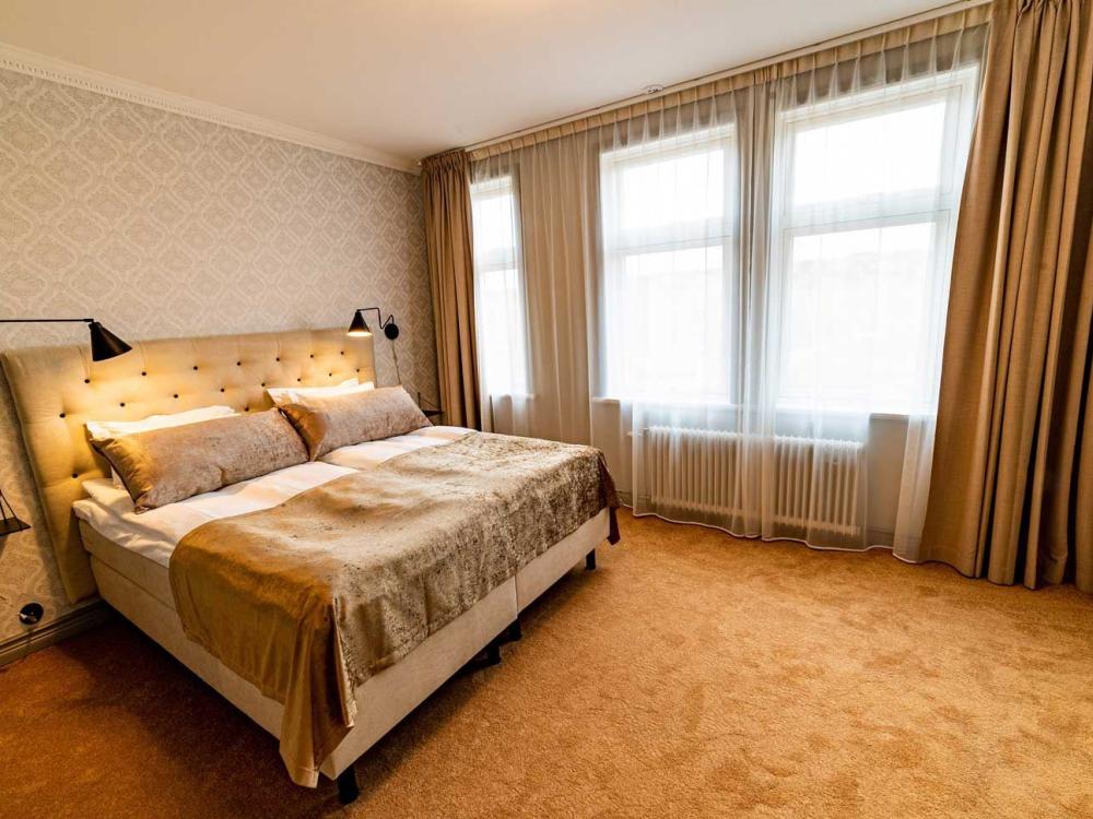 Dubbelrum med gyllenbruna färger på heltäckningsmatta, gardiner och sänggavel. 