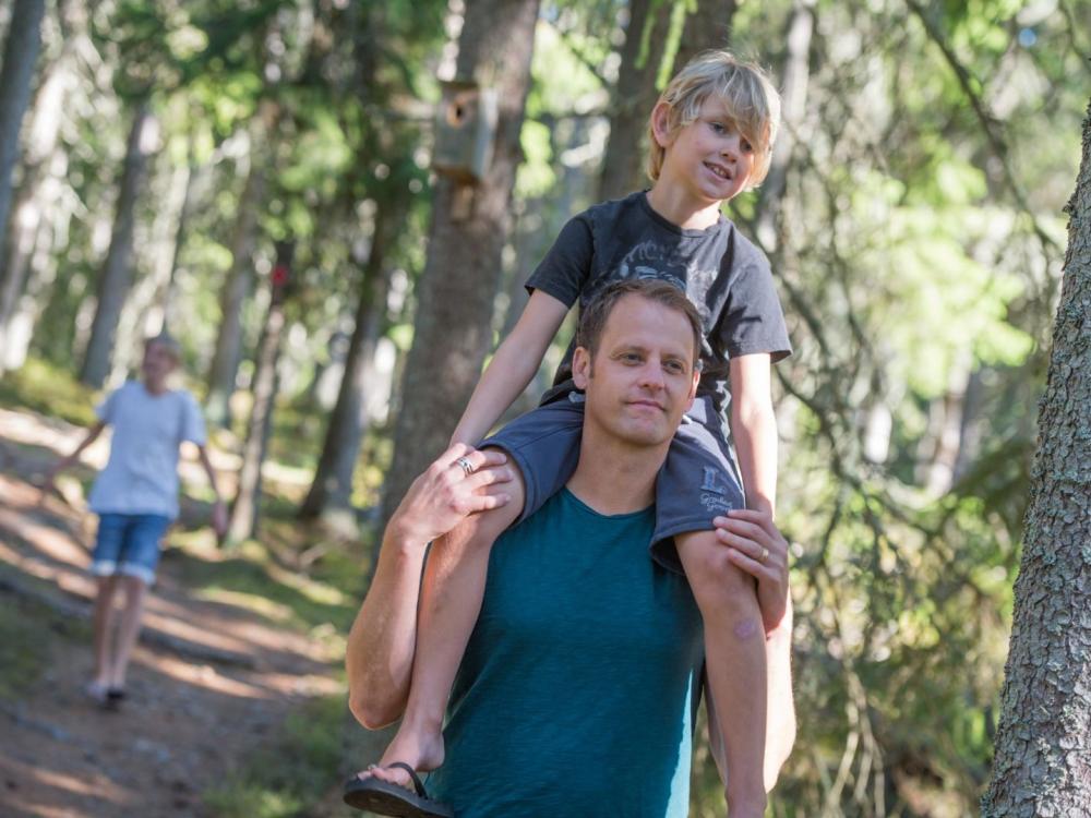 En man med ett barn på axlarna i en stig i skogen.