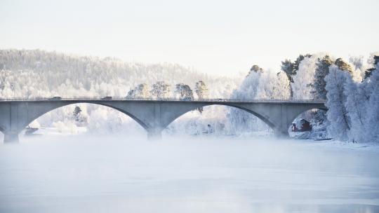 Bro över Dalälven i Leksand, det är snö på träden och is och dimma på älven.