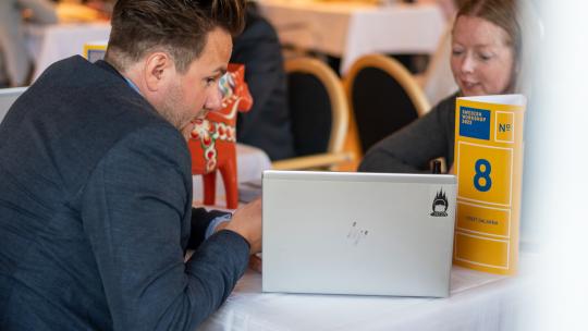 Två personer som sitter vid ett bord och kollar på en laptop.